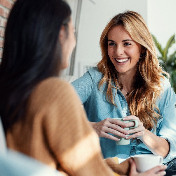Two friends smiling while enjoying cup of coffee together