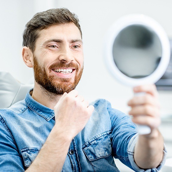Man looking at his smile after metal free dental crown placement