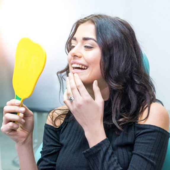 woman admiring her reflection after getting a dental bridge in Weatherford