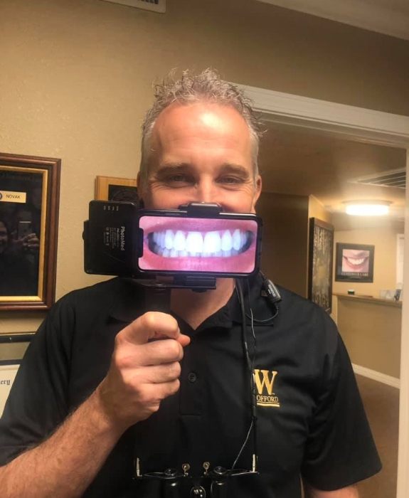 Weatherford dentist Thomas Novak D D S holding a magnifyer up to his smile