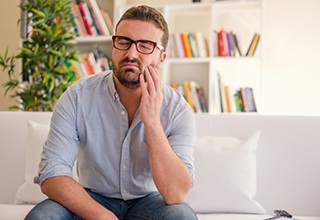 man with tooth pain sitting on couch