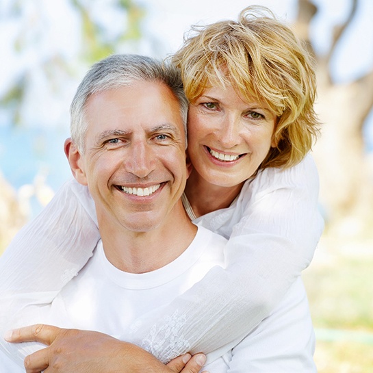 Older couple with dental implants in Weatherford hugging and smiling