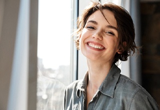 Woman by window smiling with dental implants in Weatherford, TX