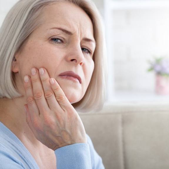a woman holding her cheek due to failed dental implant