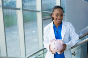 smiling dentist in Weatherford holding a pink piggy bank 