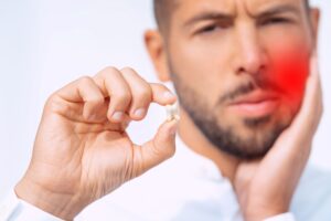 Man holding extracted tooth and touching his inflamed jaw