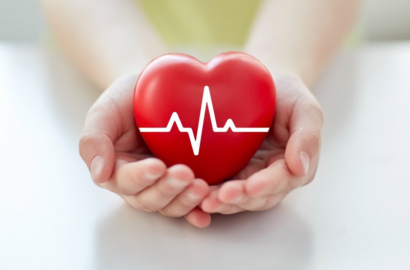 Hands holding a red heart with a cardiogram symbol